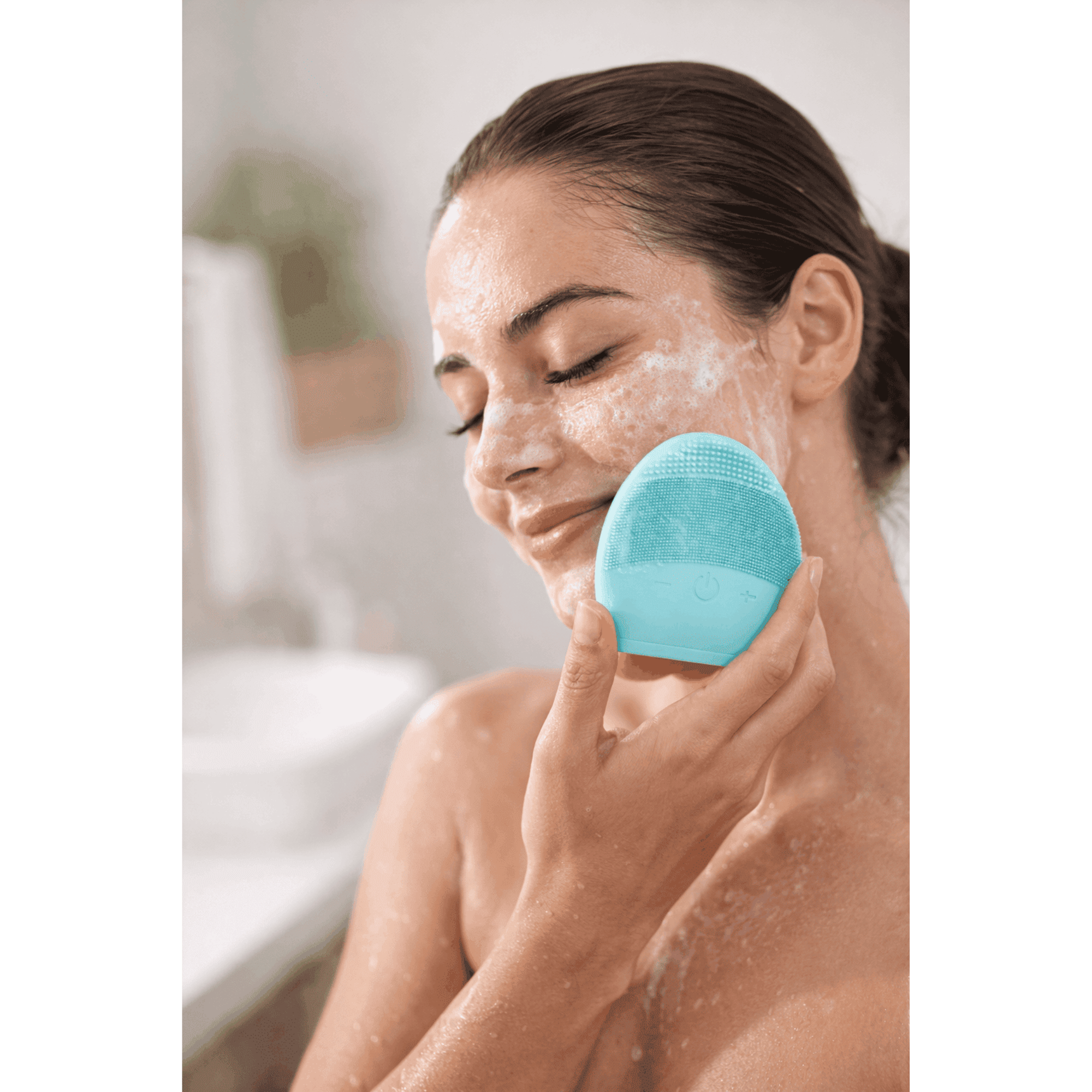 Woman using a blue facial cleansing brush on her face with a blurred indoor background