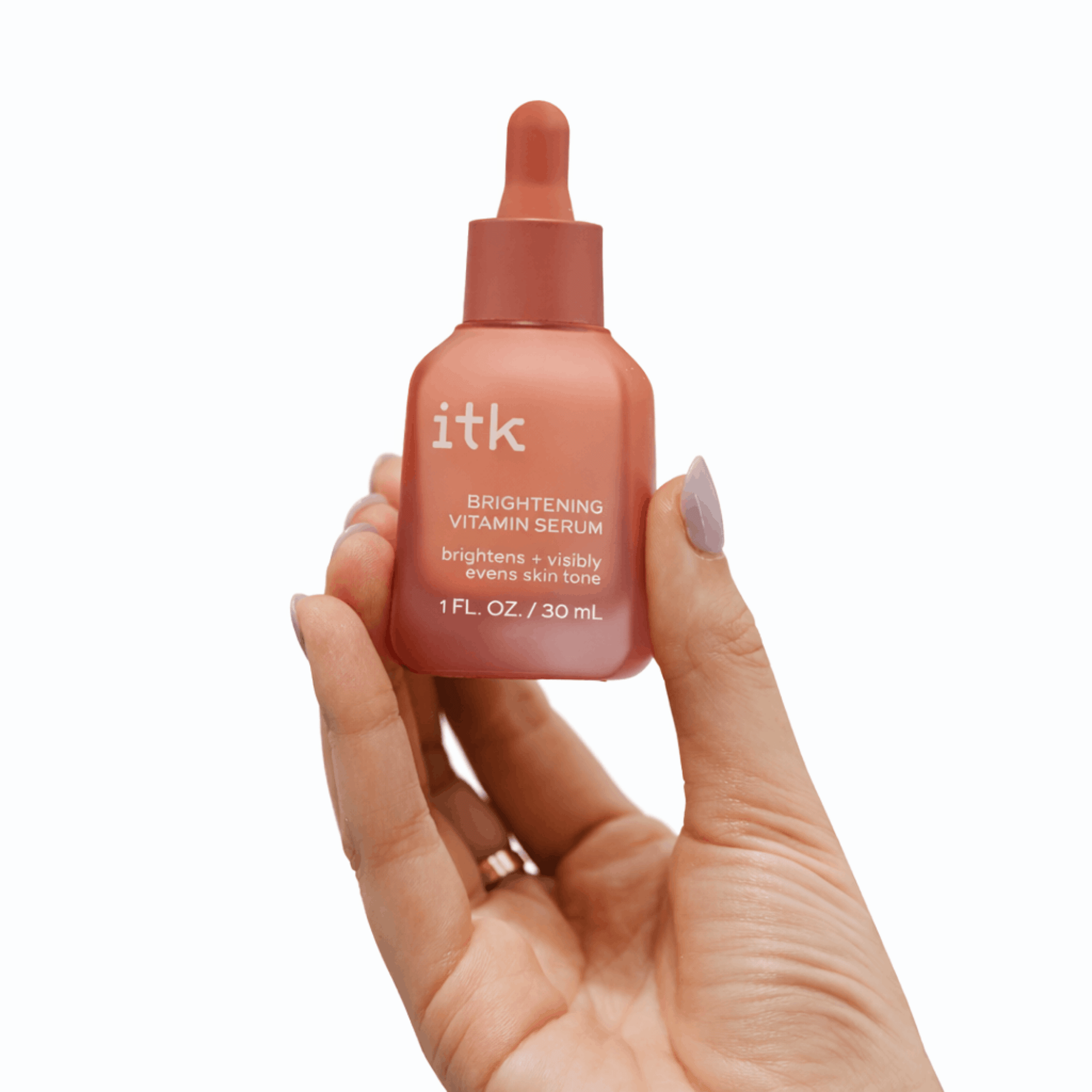 Hand holding a bottle of itk Brightening Vitamin Serum on a white background