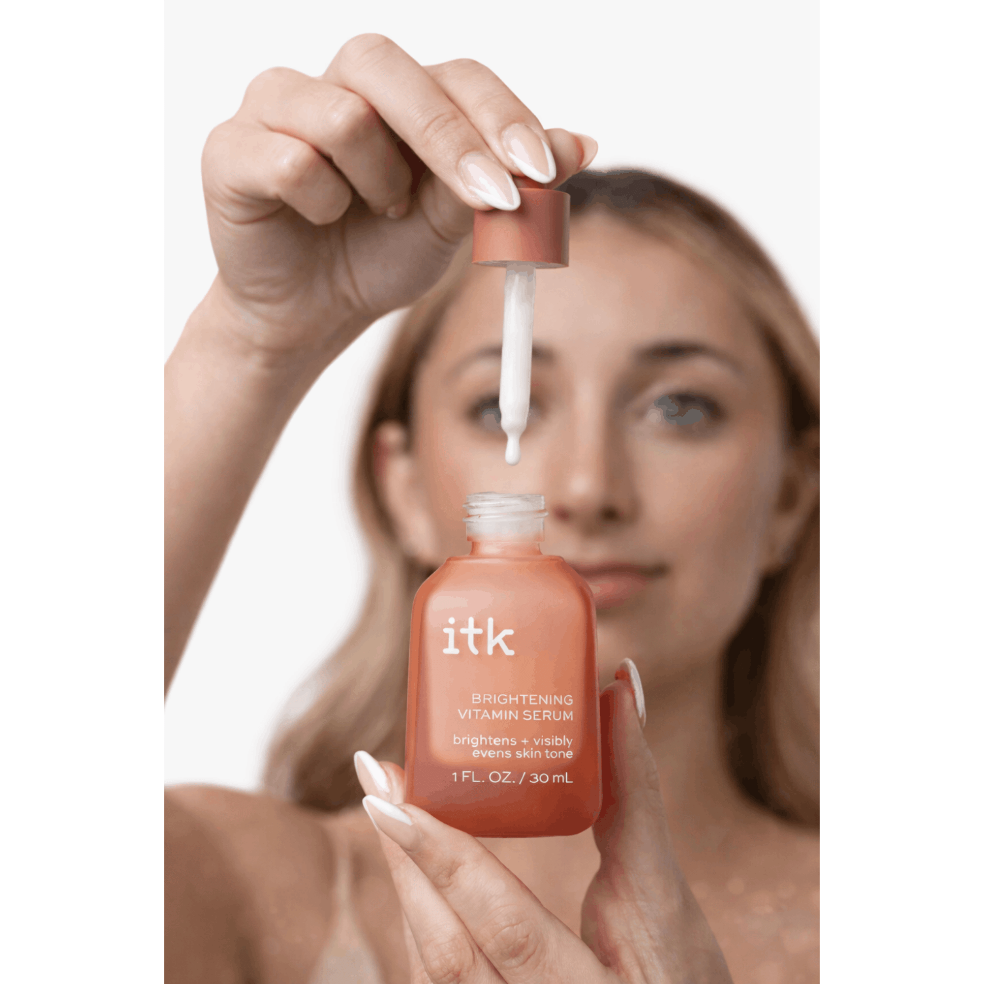 Woman holding a bottle of itk skincare product with a dropper.
