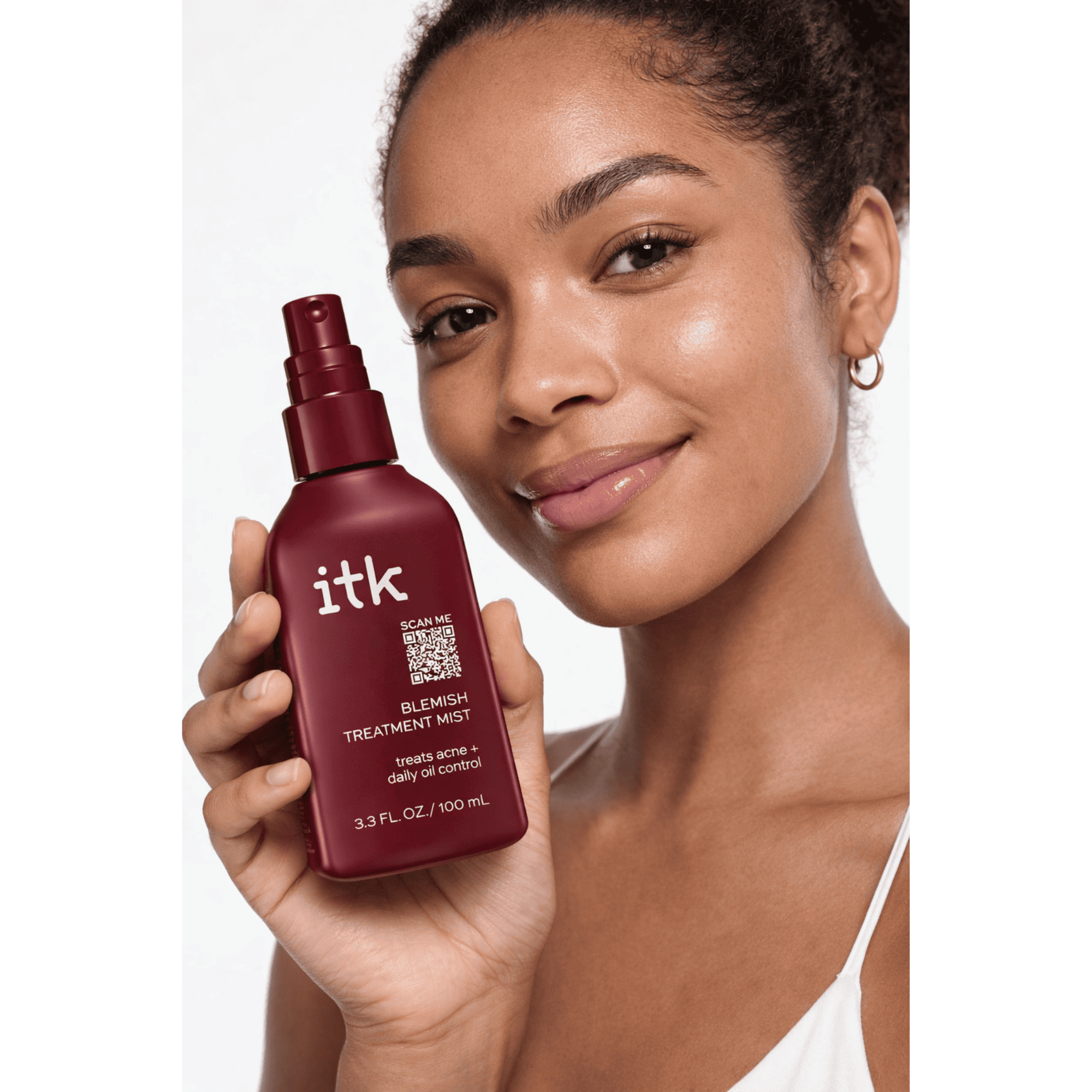 Woman holding a maroon bottle of itk skincare product against a white background