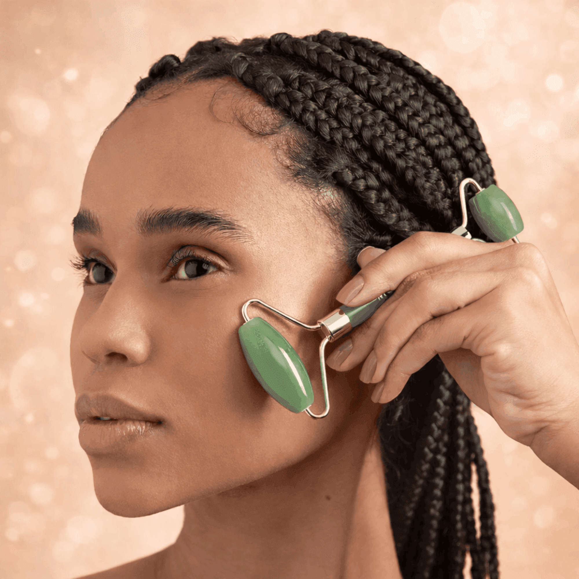 Woman using a green facial roller on her face against a beige background